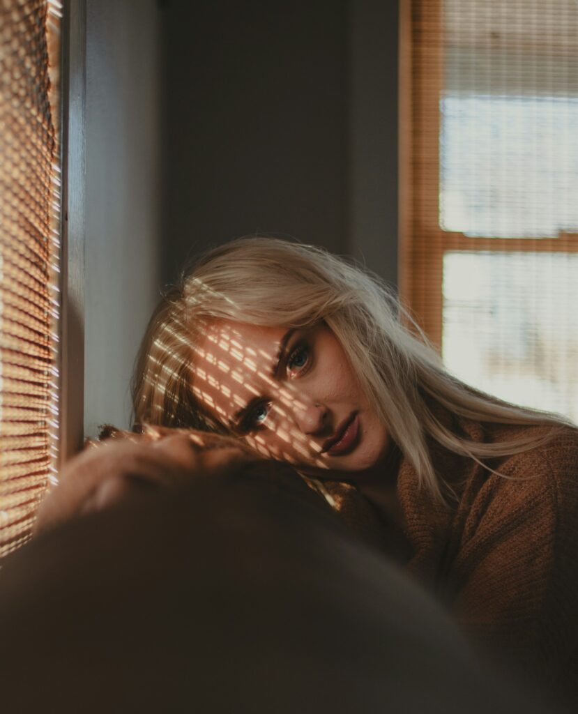 Mujer saturada junto a una ventana con luz de persianas